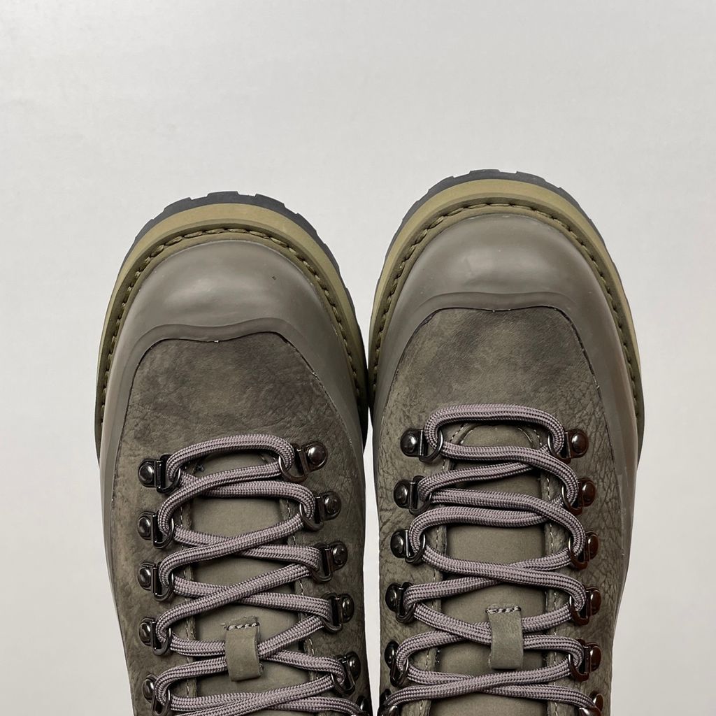 Side profile of the UMMCOR low-top hiking shoe in an earthy Army Green colorway, featuring a textured cowhide leather upper, a protective wrap-around rubber mudguard, metal D-ring lacing hardware, and a chunky lugged rubber outsole.
