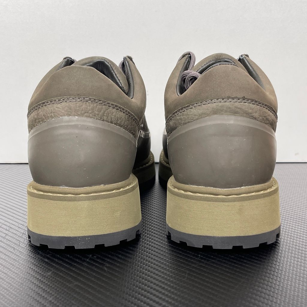 Side profile of the UMMCOR low-top hiking shoe in an earthy Army Green colorway, featuring a textured cowhide leather upper, a protective wrap-around rubber mudguard, metal D-ring lacing hardware, and a chunky lugged rubber outsole.
