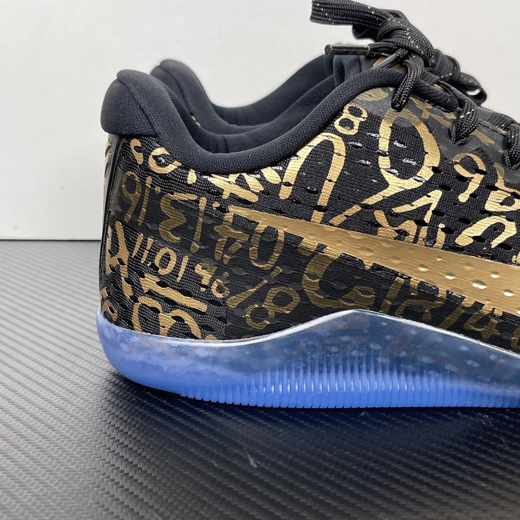 Side profile of the Nike Kobe 11 Protro basketball shoe in the Mamba Day colorway, featuring a sleek black upper with striking metallic gold Swoosh detailing, signature Kobe branding, and a translucent rubber outsole.