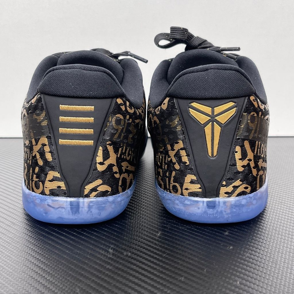 Side profile of the Nike Kobe 11 Protro basketball shoe in the Mamba Day colorway, featuring a sleek black upper with striking metallic gold Swoosh detailing, signature Kobe branding, and a translucent rubber outsole.