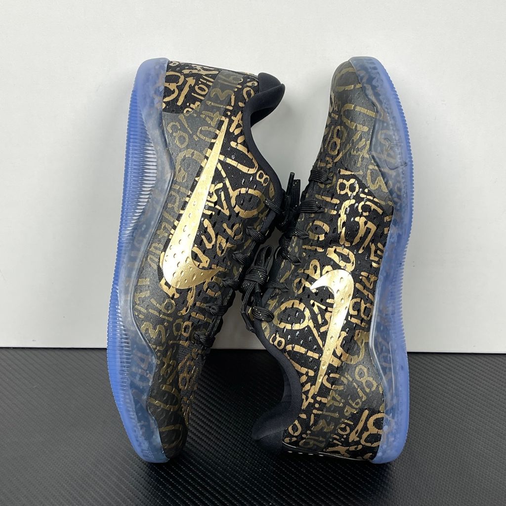 Side profile of the Nike Kobe 11 Protro basketball shoe in the Mamba Day colorway, featuring a sleek black upper with striking metallic gold Swoosh detailing, signature Kobe branding, and a translucent rubber outsole.