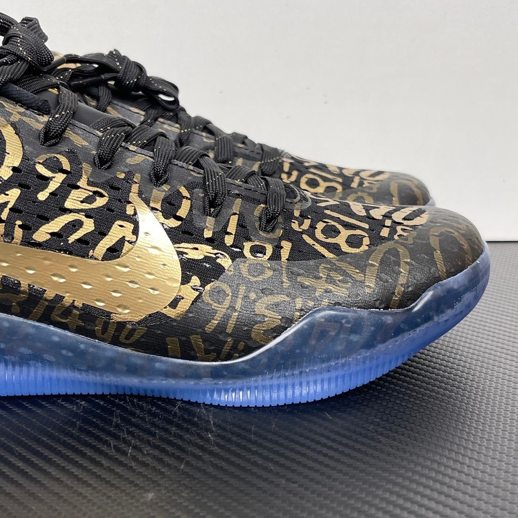 Side profile of the Nike Kobe 11 Protro basketball shoe in the Mamba Day colorway, featuring a sleek black upper with striking metallic gold Swoosh detailing, signature Kobe branding, and a translucent rubber outsole.