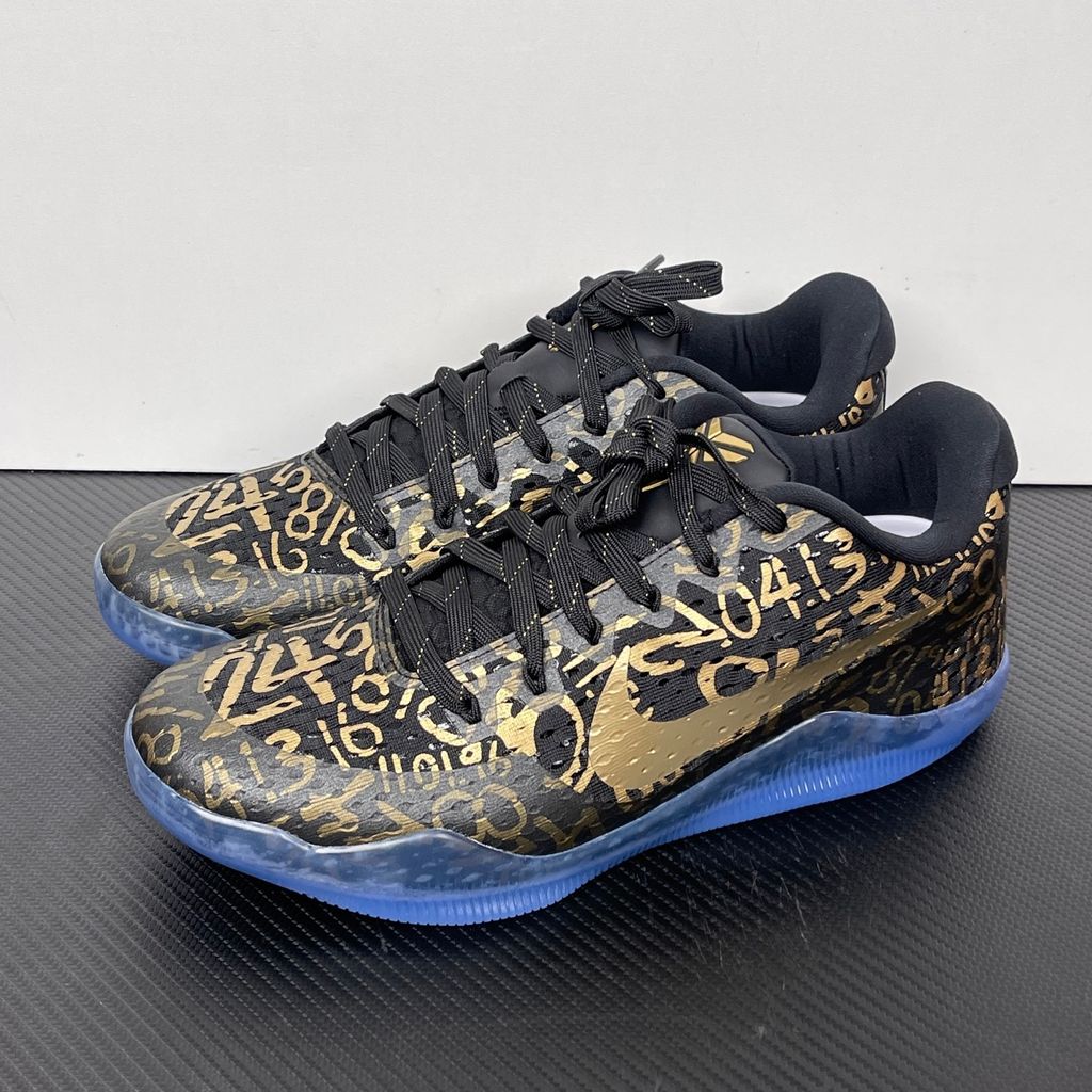 Side profile of the Nike Kobe 11 Protro basketball shoe in the Mamba Day colorway, featuring a sleek black upper with striking metallic gold Swoosh detailing, signature Kobe branding, and a translucent rubber outsole.