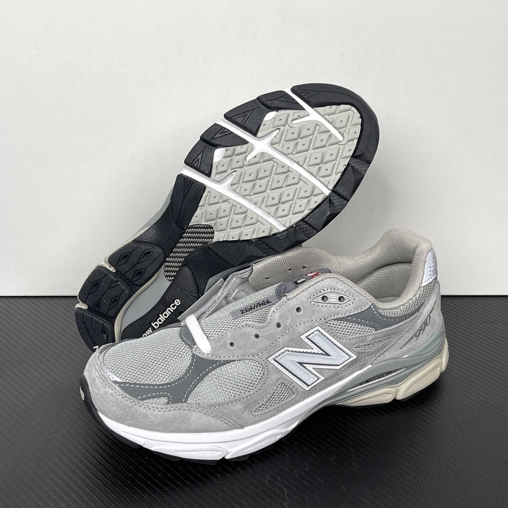 Side profile of the classic New Balance 990v3 Made in USA sneaker featuring a premium grey pigskin suede and mesh upper, silver reflective 'N' logo, and a split white and grey ENCAP midsole.