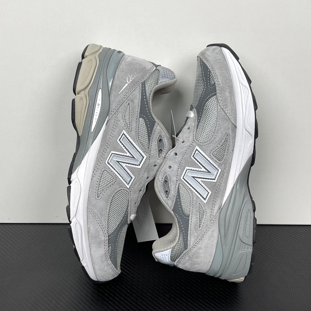 Side profile of the classic New Balance 990v3 Made in USA sneaker featuring a premium grey pigskin suede and mesh upper, silver reflective 'N' logo, and a split white and grey ENCAP midsole.