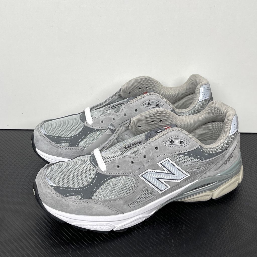 Side profile of the classic New Balance 990v3 Made in USA sneaker featuring a premium grey pigskin suede and mesh upper, silver reflective 'N' logo, and a split white and grey ENCAP midsole.