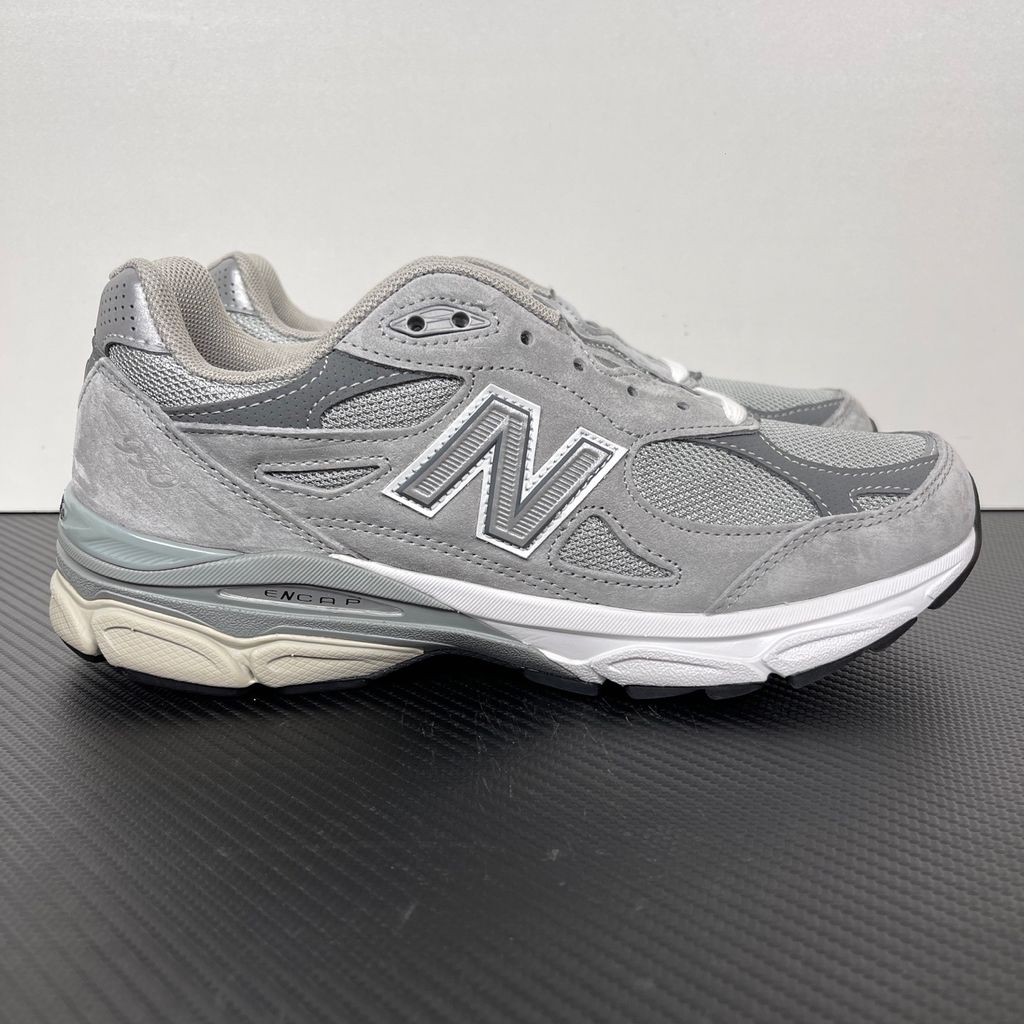 Side profile of the classic New Balance 990v3 Made in USA sneaker featuring a premium grey pigskin suede and mesh upper, silver reflective 'N' logo, and a split white and grey ENCAP midsole.