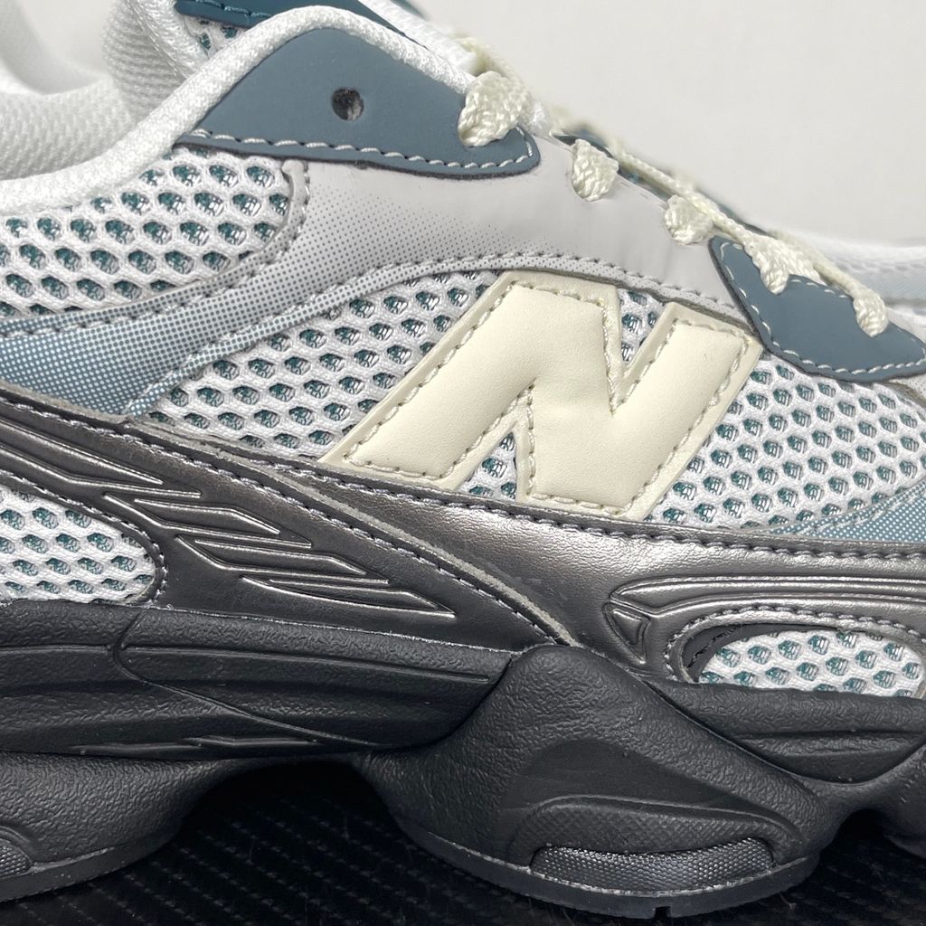 Side profile of the New Balance 9060 sneaker featuring a white open-mesh upper, striking metallic silver overlays, a cream 'N' logo, and a dramatic, chunky black wavy midsole with ABZORB cushioning.