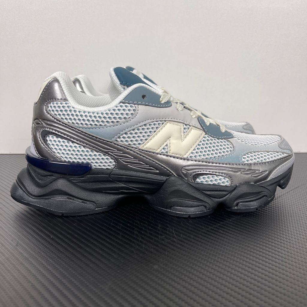 Side profile of the New Balance 9060 sneaker featuring a white open-mesh upper, striking metallic silver overlays, a cream 'N' logo, and a dramatic, chunky black wavy midsole with ABZORB cushioning.