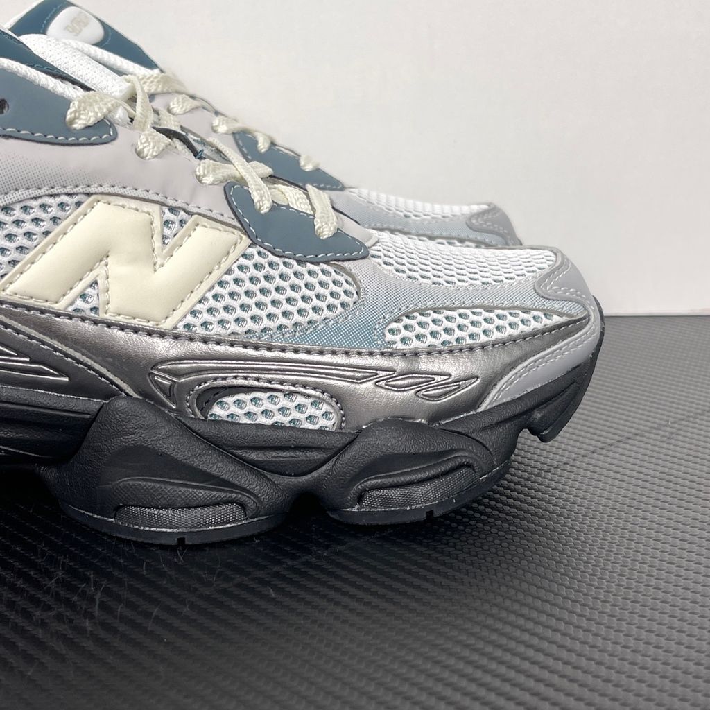 Side profile of the New Balance 9060 sneaker featuring a white open-mesh upper, striking metallic silver overlays, a cream 'N' logo, and a dramatic, chunky black wavy midsole with ABZORB cushioning.