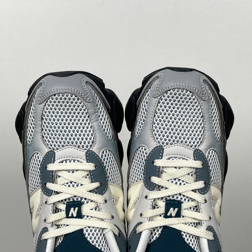 Side profile of the New Balance 9060 sneaker featuring a white open-mesh upper, striking metallic silver overlays, a cream 'N' logo, and a dramatic, chunky black wavy midsole with ABZORB cushioning.