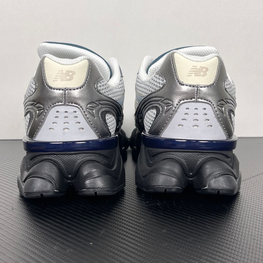 Side profile of the New Balance 9060 sneaker featuring a white open-mesh upper, striking metallic silver overlays, a cream 'N' logo, and a dramatic, chunky black wavy midsole with ABZORB cushioning.