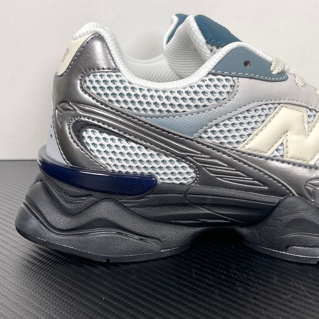 Side profile of the New Balance 9060 sneaker featuring a white open-mesh upper, striking metallic silver overlays, a cream 'N' logo, and a dramatic, chunky black wavy midsole with ABZORB cushioning.