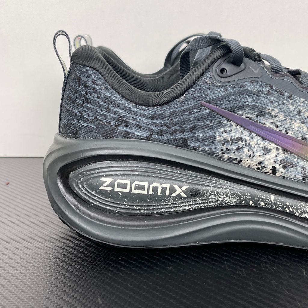 Side profile of the Nike Vomero Plus sneaker in a dark Anthracite and Black colorway with subtle Oatmeal accents, featuring a layered mesh and synthetic upper, a structured midfoot cage, and a responsive Zoom Air midsole.
