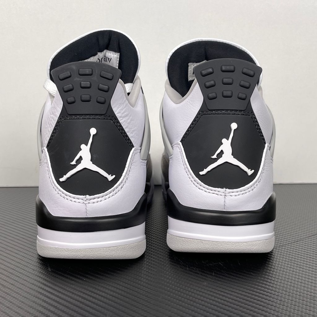 Side profile of the Air Jordan 4 Retro 'Military Black' sneaker featuring a crisp white tumbled leather upper, a light grey suede toe wrap, contrasting black TPU support wings and heel tab, and a white midsole with a visible Air unit.