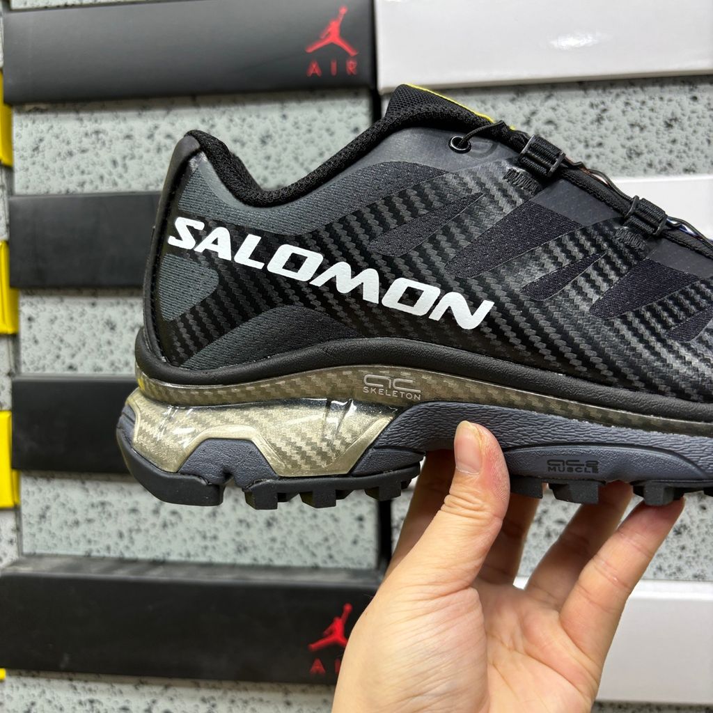 Side profile of the Salomon XT-4 OG trail running sneaker in a sleek all-black colorway, featuring a durable TPU film mesh upper, a Quicklace system, and an aggressive Contagrip rubber outsole.