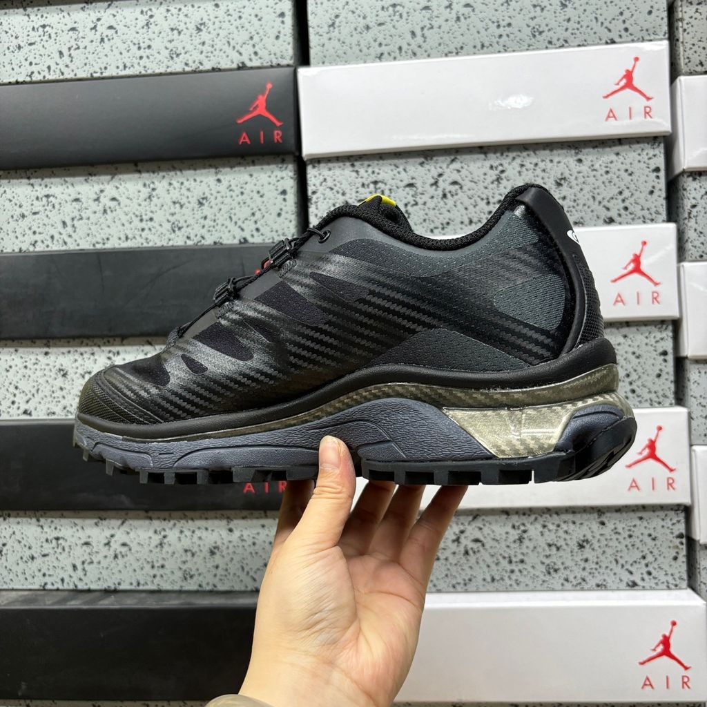 Side profile of the Salomon XT-4 OG trail running sneaker in a sleek all-black colorway, featuring a durable TPU film mesh upper, a Quicklace system, and an aggressive Contagrip rubber outsole.