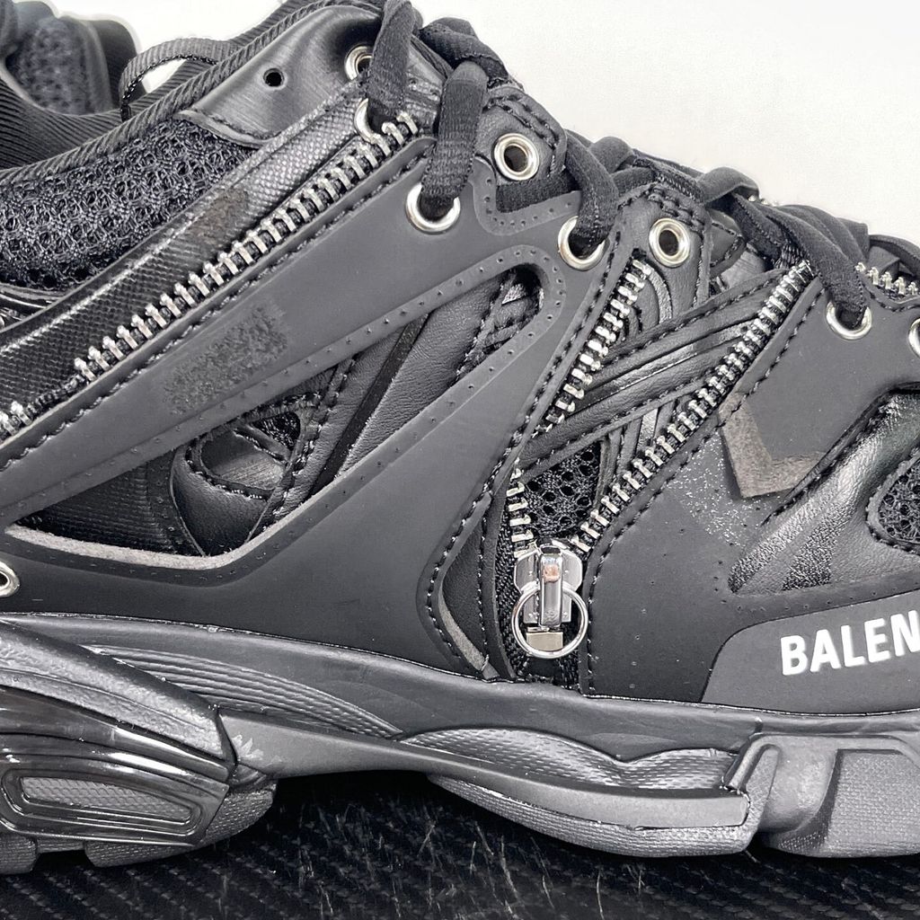 Side profile of the Balenciaga Track LED sneaker in an all-black colorway, featuring a complex layered mesh and synthetic upper, metallic zipper embellishments across the side panels, a chunky augmented sole, and a built-in LED heel display.