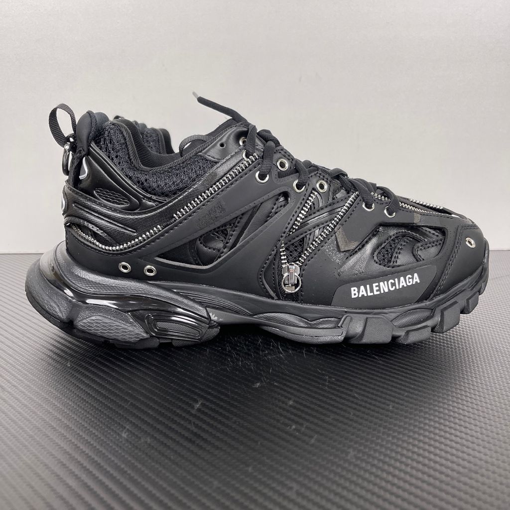 Side profile of the Balenciaga Track LED sneaker in an all-black colorway, featuring a complex layered mesh and synthetic upper, metallic zipper embellishments across the side panels, a chunky augmented sole, and a built-in LED heel display.