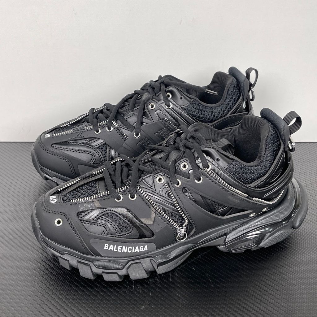 Side profile of the Balenciaga Track LED sneaker in an all-black colorway, featuring a complex layered mesh and synthetic upper, metallic zipper embellishments across the side panels, a chunky augmented sole, and a built-in LED heel display.