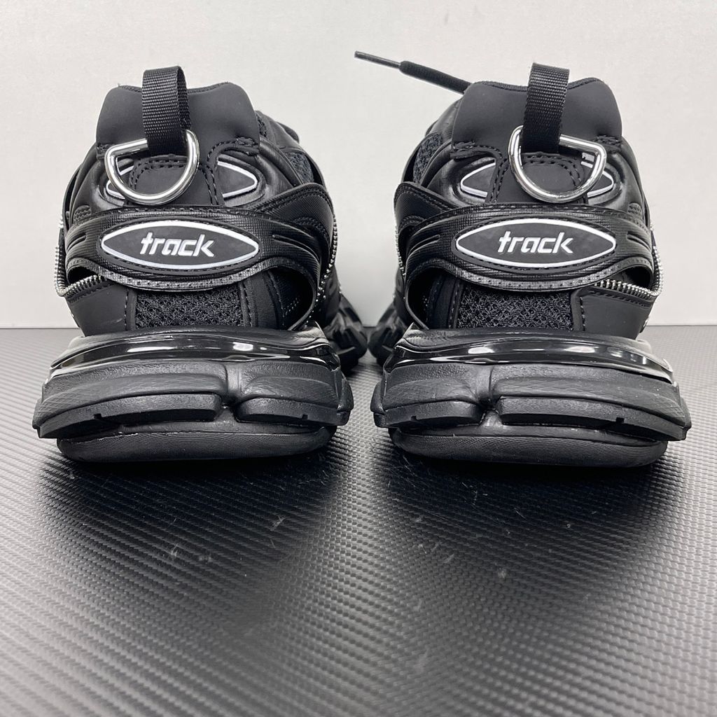 Side profile of the Balenciaga Track LED sneaker in an all-black colorway, featuring a complex layered mesh and synthetic upper, metallic zipper embellishments across the side panels, a chunky augmented sole, and a built-in LED heel display.