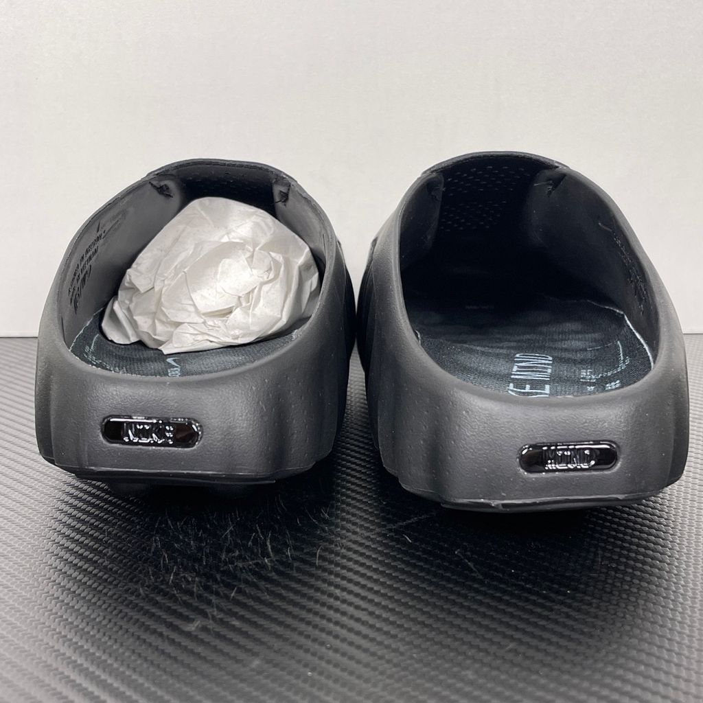 Side profile of the Nike Mind 001 Slide in a sleek Triple Black colorway, featuring a seamless, minimalist foam construction, a contoured footbed, and a durable traction outsole.