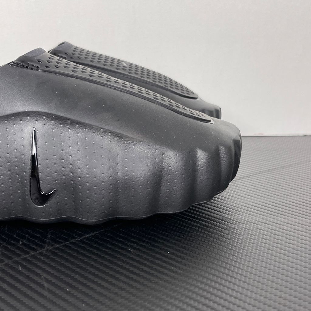 Side profile of the Nike Mind 001 Slide in a sleek Triple Black colorway, featuring a seamless, minimalist foam construction, a contoured footbed, and a durable traction outsole.