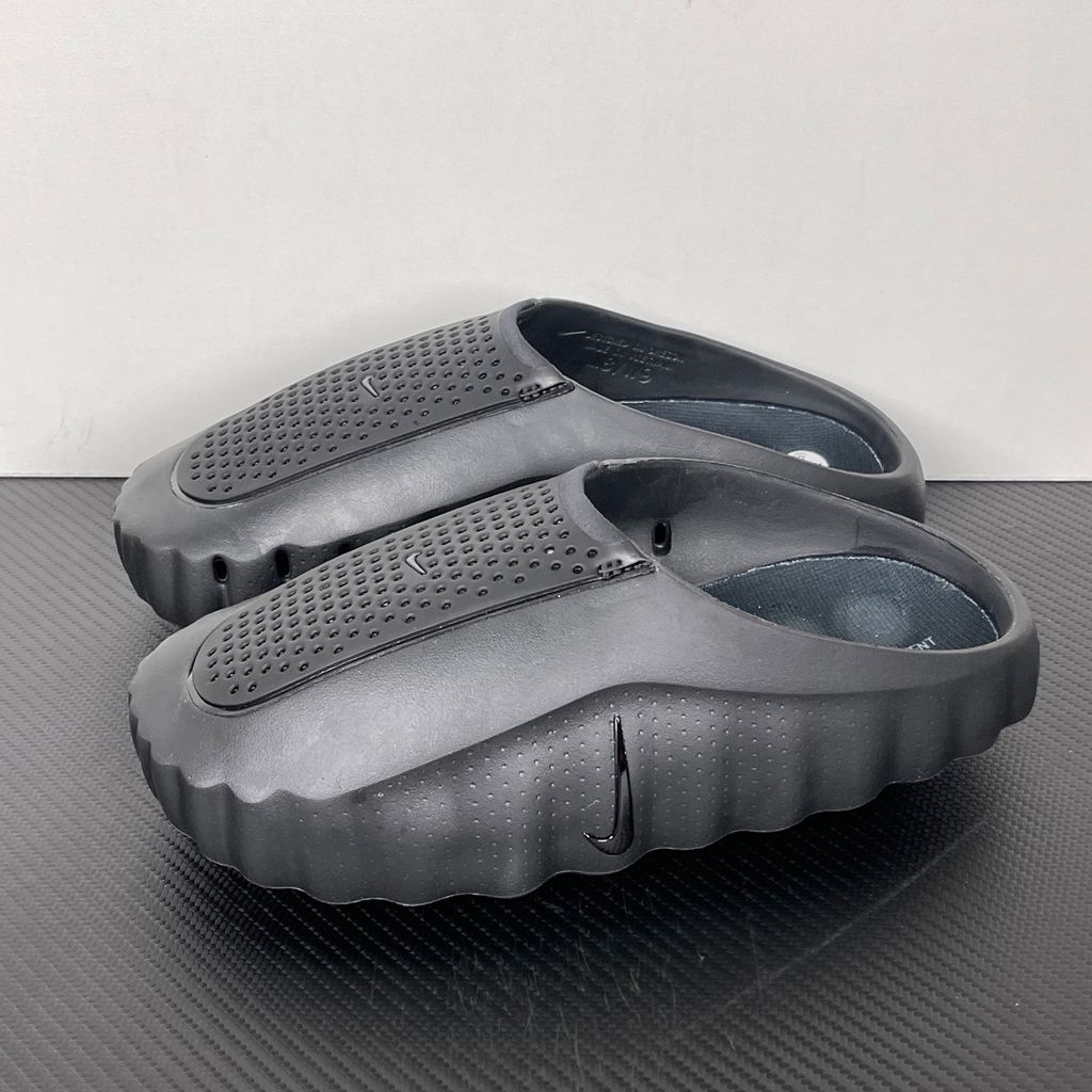 Side profile of the Nike Mind 001 Slide in a sleek Triple Black colorway, featuring a seamless, minimalist foam construction, a contoured footbed, and a durable traction outsole.