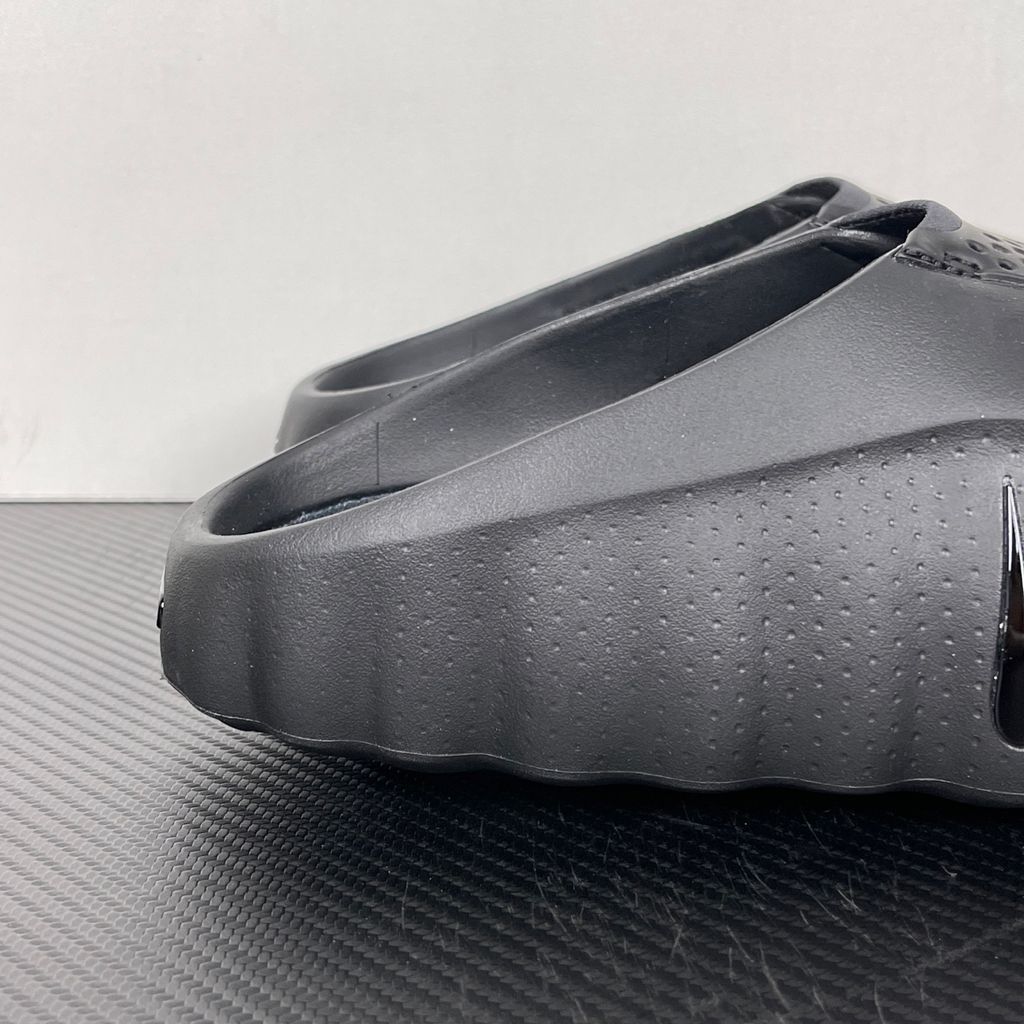 Side profile of the Nike Mind 001 Slide in a sleek Triple Black colorway, featuring a seamless, minimalist foam construction, a contoured footbed, and a durable traction outsole.