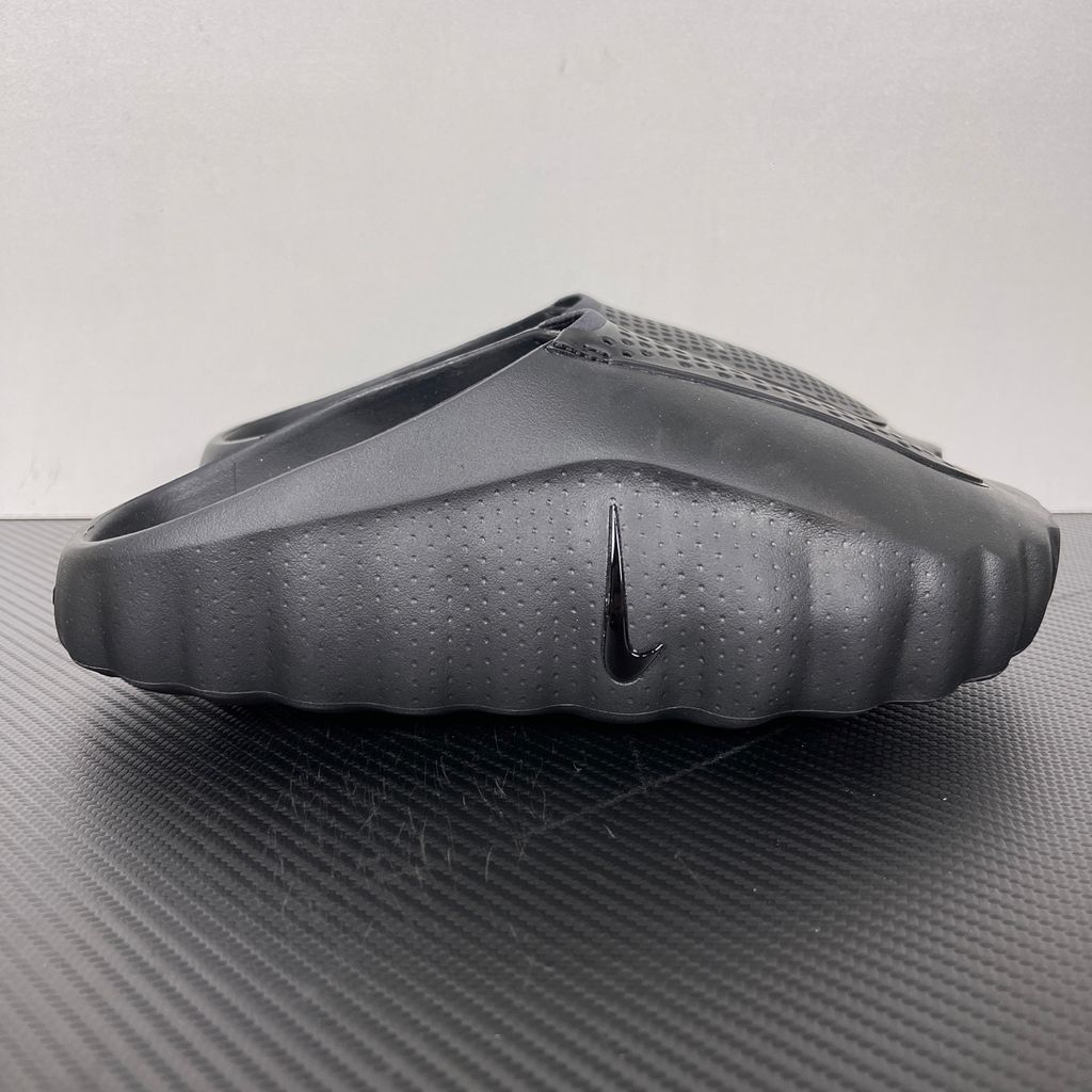 Side profile of the Nike Mind 001 Slide in a sleek Triple Black colorway, featuring a seamless, minimalist foam construction, a contoured footbed, and a durable traction outsole.