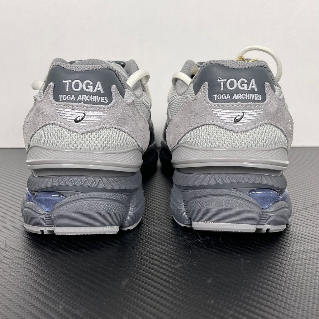 Side profile of the collaborative ASICS x TOGA Gel-Cumulus 16 sneaker in a Grey, Black, and Pure Silver colorway, featuring a breathable mesh upper, striking metallic silver overlays, sleek black accents, and a sculpted GEL-cushioned midsole.