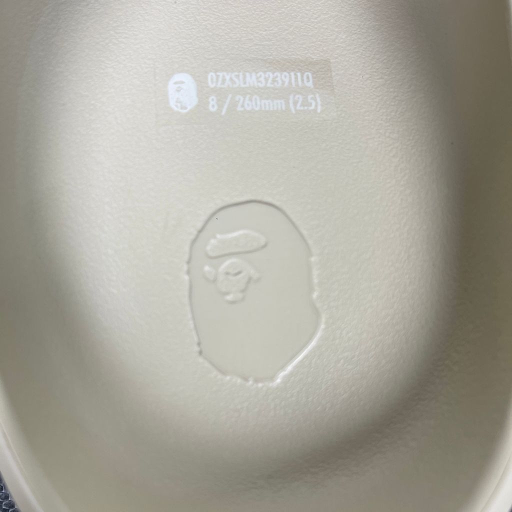 Side profile of the beige A Bathing Ape (BAPE) foam slide (image_889658.jpg), featuring a chunky molded silhouette, a smooth slip-on upper, and deeply debossed signature ape camo patterns wrapping around the midsole and foot strap.