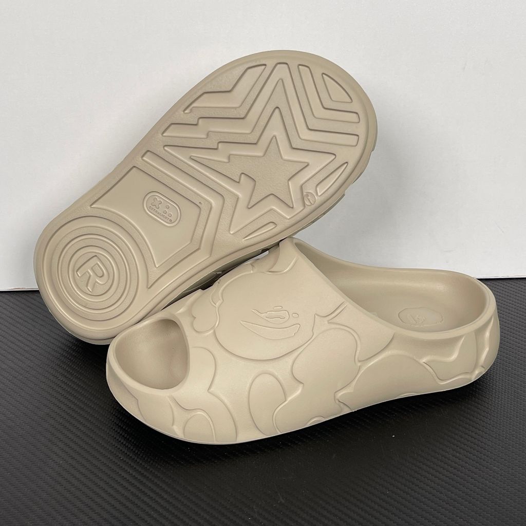 Side profile of the beige A Bathing Ape (BAPE) foam slide (image_889658.jpg), featuring a chunky molded silhouette, a smooth slip-on upper, and deeply debossed signature ape camo patterns wrapping around the midsole and foot strap.