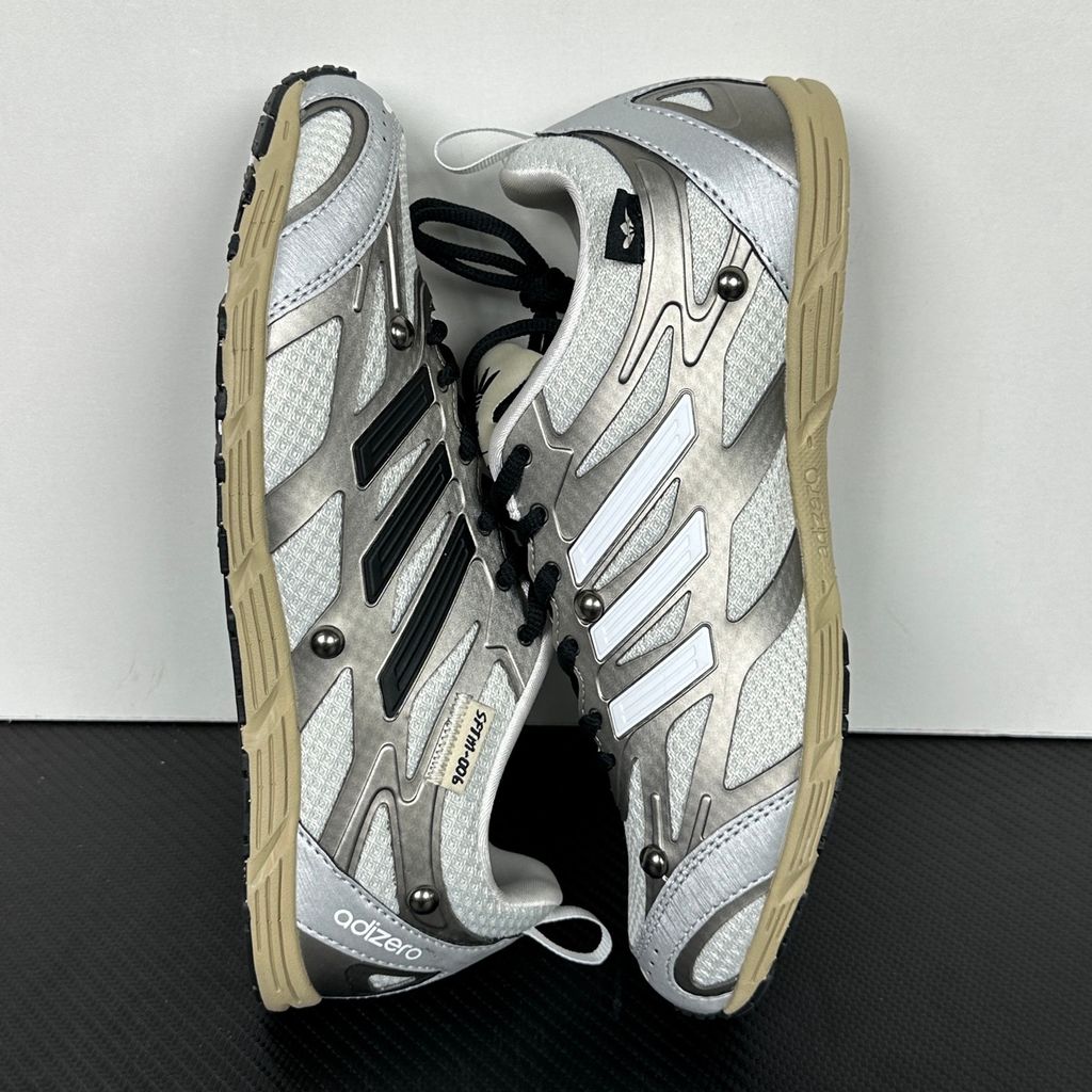 Side profile of the adidas Adizero PR x Song for the Mute collaborative sneaker featuring a crisp white breathable mesh base, gleaming silver metallic synthetic overlays, signature raw-edge and frayed textile accents, and a lightweight cushioned midsole.