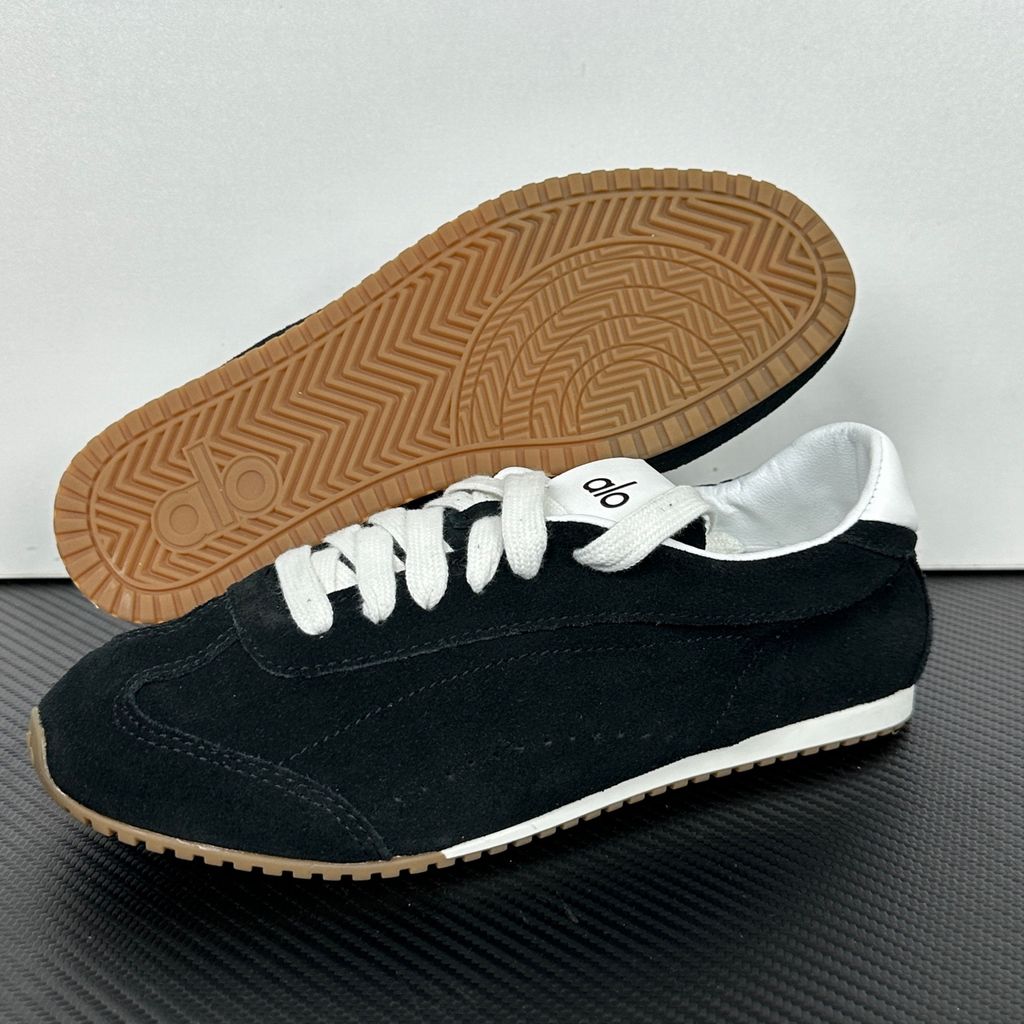 The ALO Sunset Sneaker Black/Ivory (A0891U) is a low-profile lifestyle sneaker inspired by the polished street style of Sunset Boulevard. It combines a black suede upper, contrasting Ivory details, recovery-foam cushioning and a flat gum-rubber outsole.