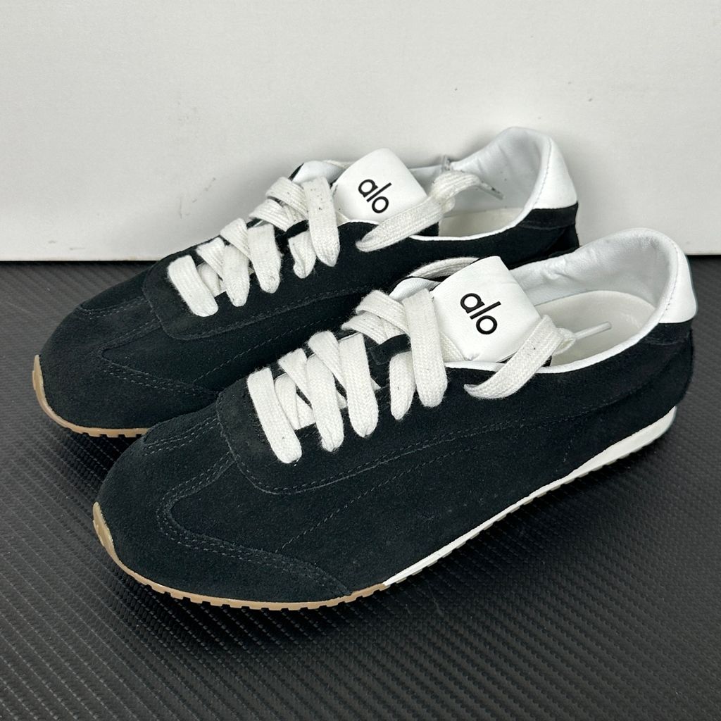The ALO Sunset Sneaker Black/Ivory (A0891U) is a low-profile lifestyle sneaker inspired by the polished street style of Sunset Boulevard. It combines a black suede upper, contrasting Ivory details, recovery-foam cushioning and a flat gum-rubber outsole.