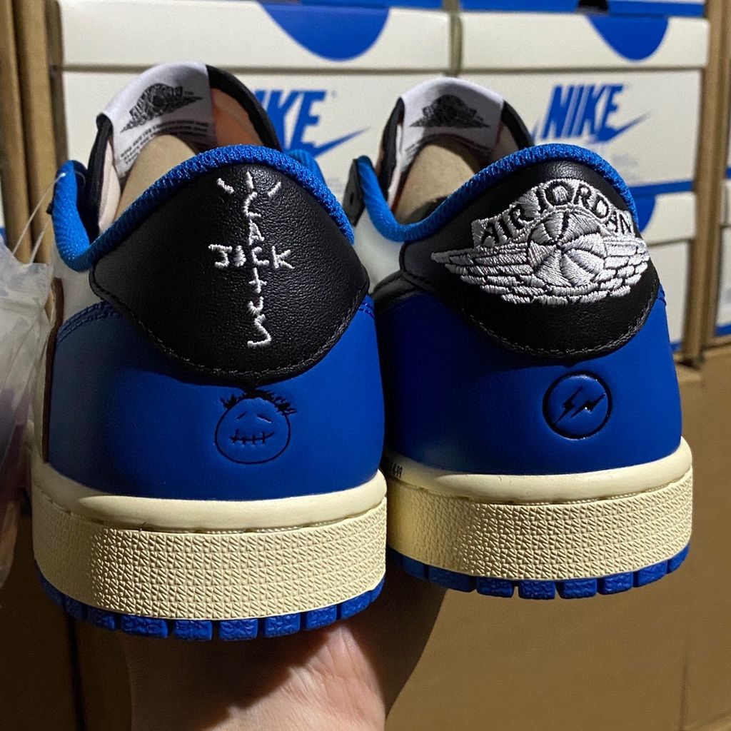 Shop Fragment Design x Travis Scott x Air Jordan 1 Low OG SP DM7866-140 in White, Black, Royal and Sail with reverse Swoosh and collaborative heel branding.