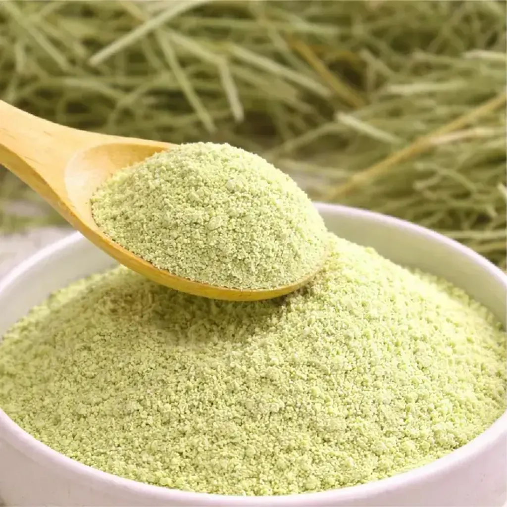 A wooden spoon of Bubble & Pea hay powder beside a bowl, with long hay behind it