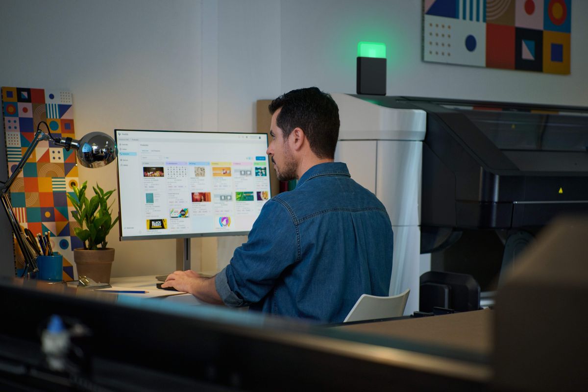 Operator preparing print jobs in ONYX RIP software beside a large format printer