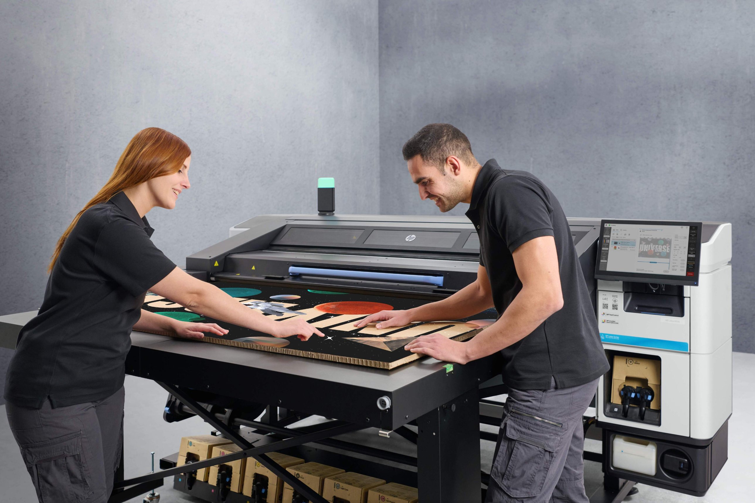 Two operators loading a printed board onto an HP Latex printer