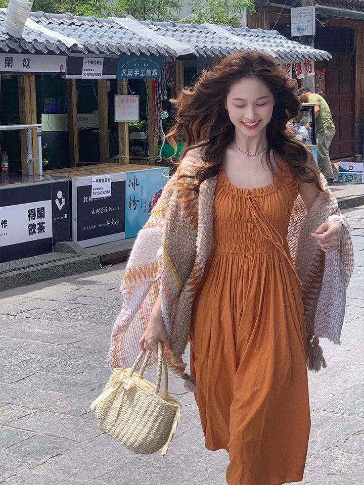 橘棕色無袖長洋裝，搭配針織外套與草編包的街頭穿搭