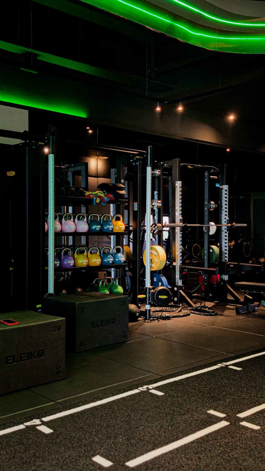 A gym floor with Eleiko racks, kettlebells and plyo boxes under green lighting