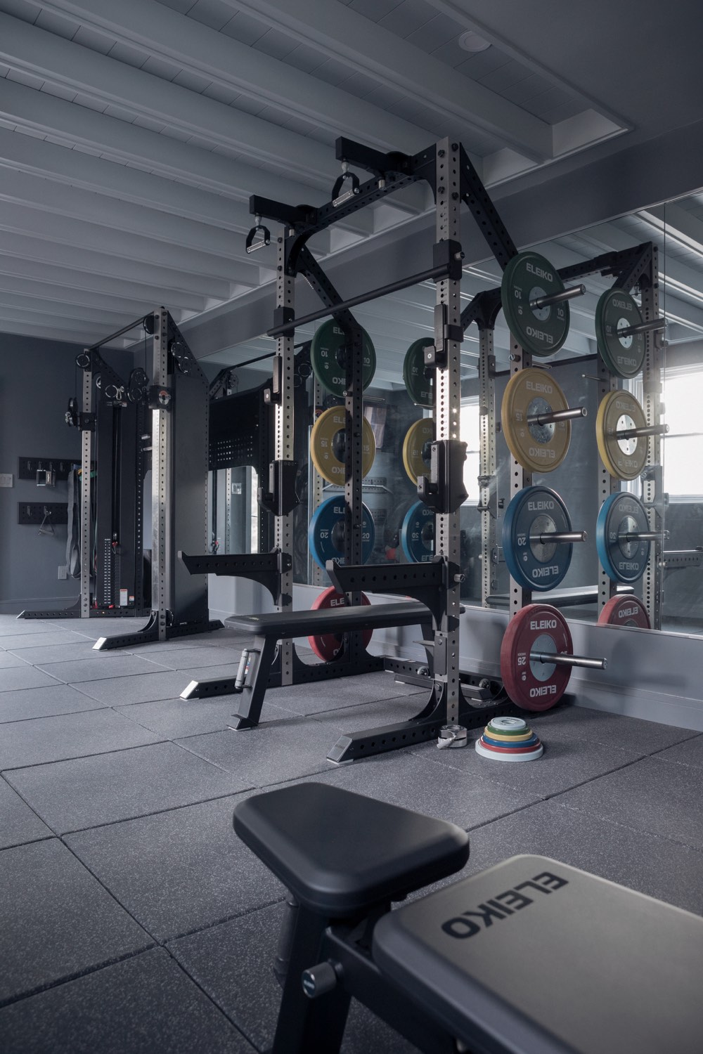 A grey home gym with Eleiko racks, coloured plates and a bench