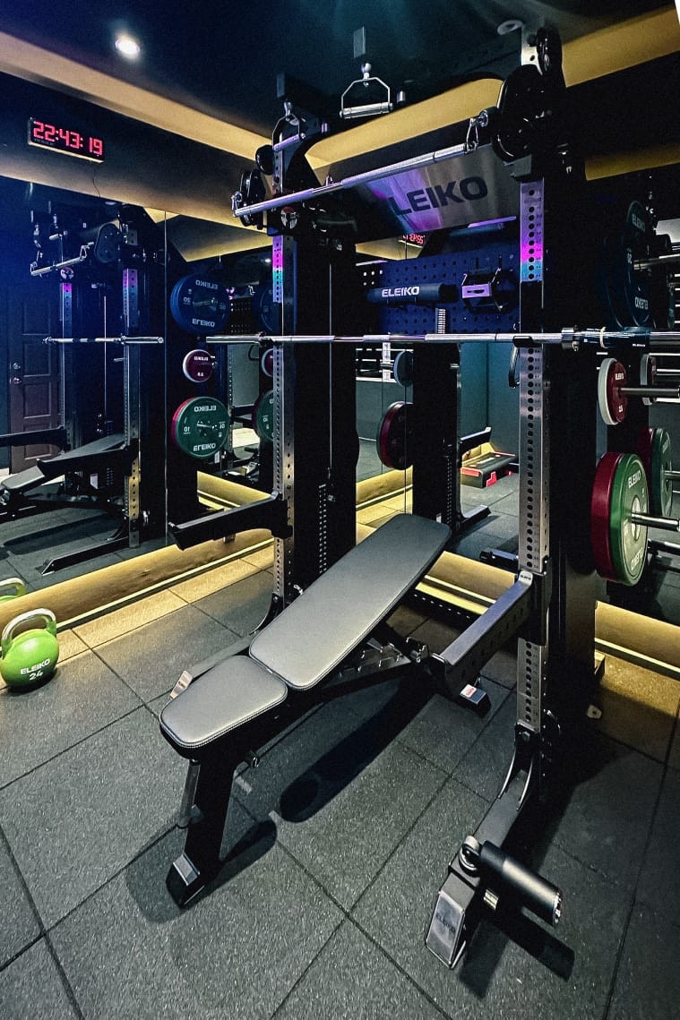 A home gym with an Eleiko rack, bench and plates under coloured lighting