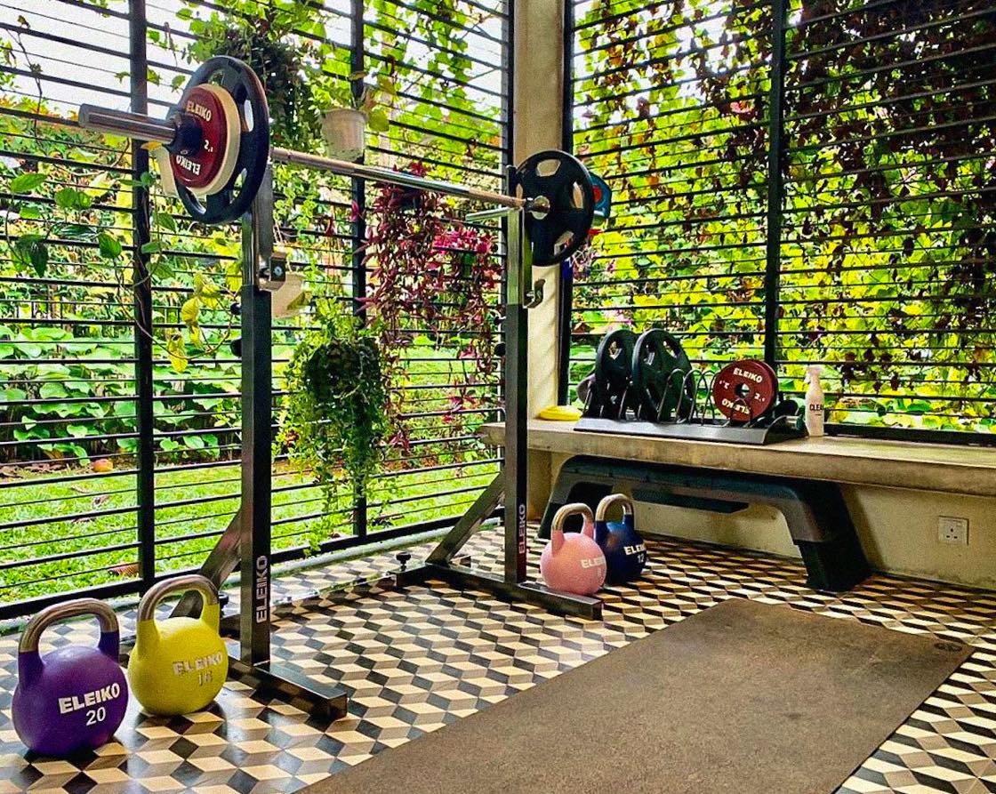 An Eleiko squat stand with a loaded bar and kettlebells on a garden patio