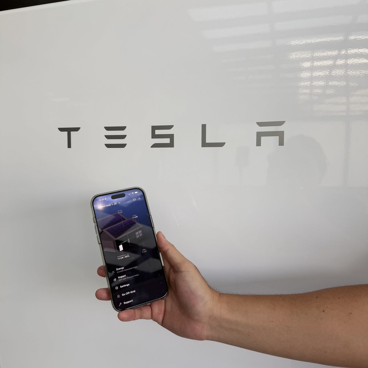 手持手機顯示 Tesla App 的 Powerwall 能源流動畫面