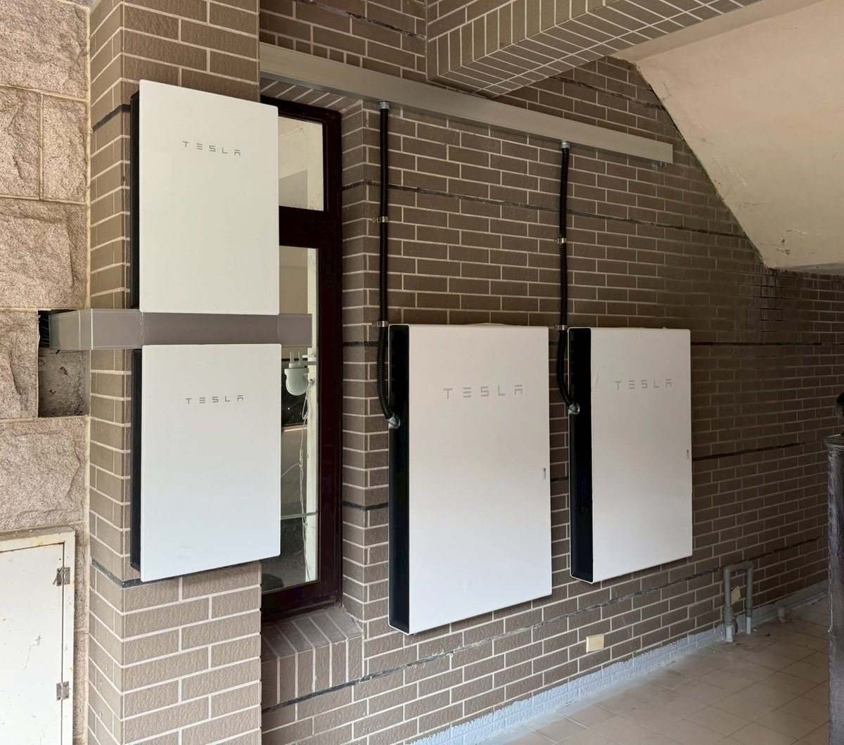 崧象智能安裝實績：騎樓磚牆與柱面上安裝的 Tesla Powerwall，線路收在上方線槽