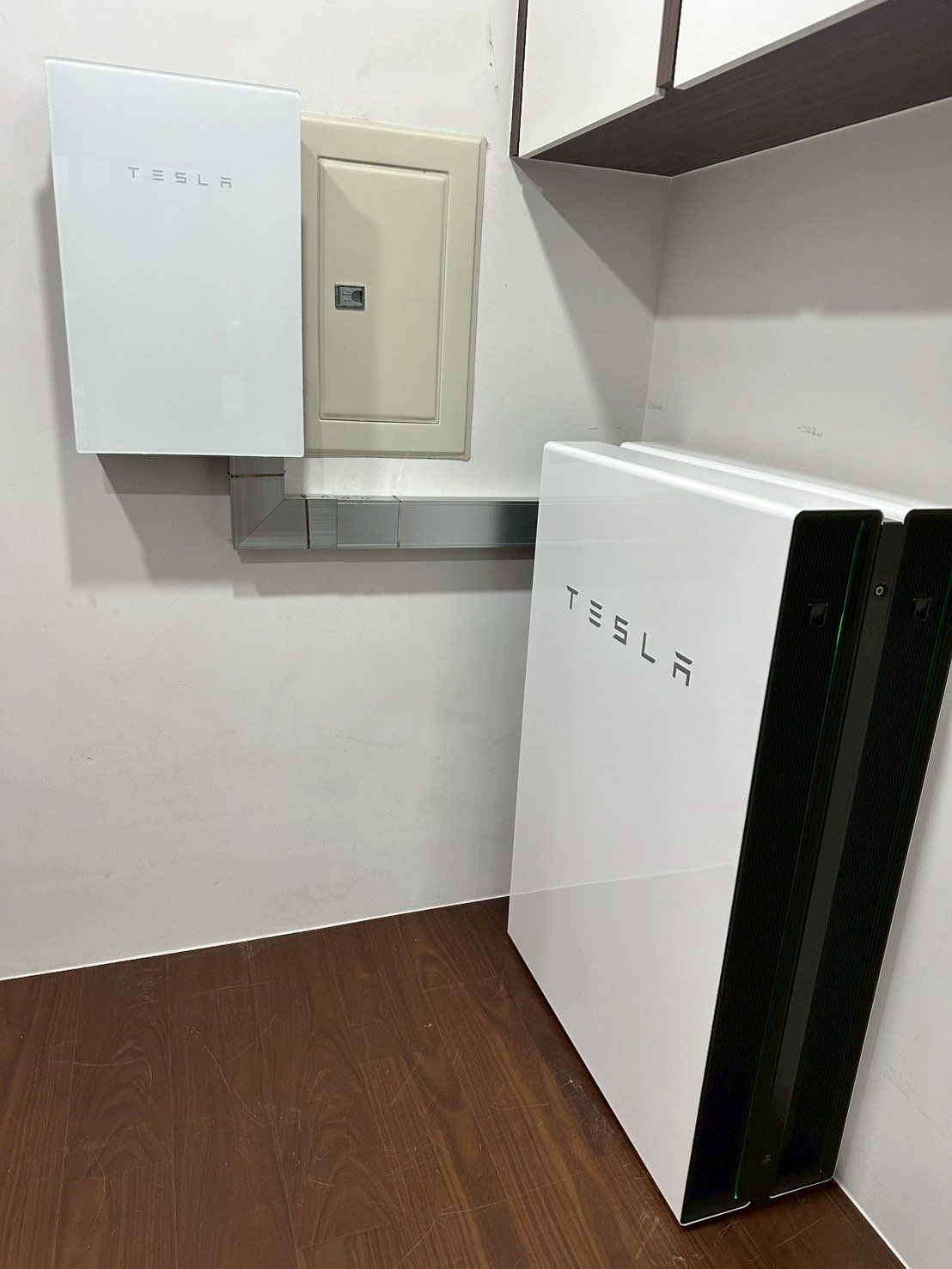 崧象智能的室內安裝實績：Tesla Backup Gateway 與配電箱壁掛在左側牆面，線槽接到右側落地安裝的 Powerwall×2，側邊綠色燈條亮起