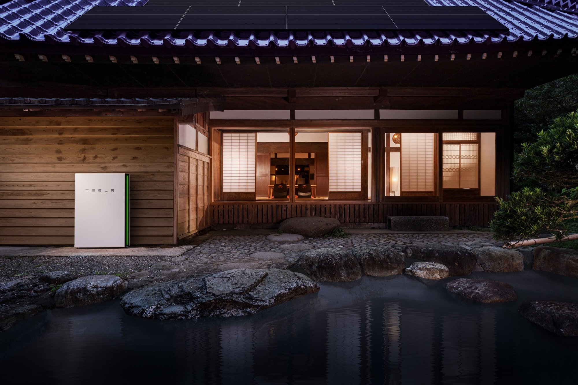 Tesla 官方生活風格圖:夜晚的日式木造住宅,外牆旁落地安裝的 Powerwall 側邊燈條亮起,室內燈光明亮,屋頂裝有太陽能板