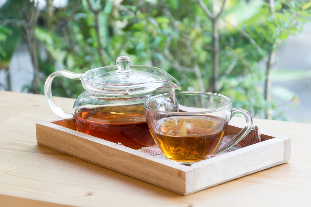 Glass teapot and cups of tea on a wooden tray